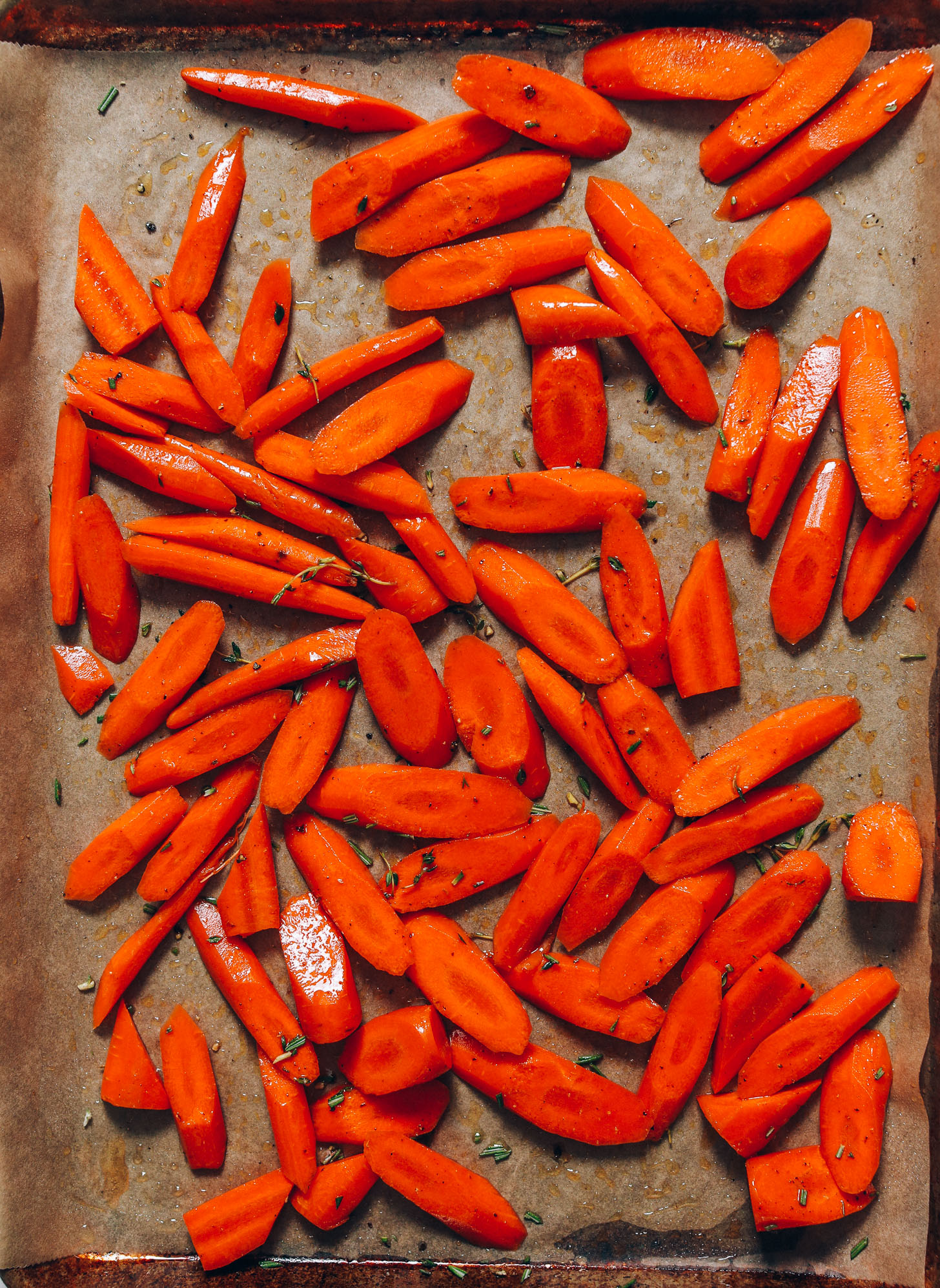 Sliced carrots on a baking sheet with fresh thyme