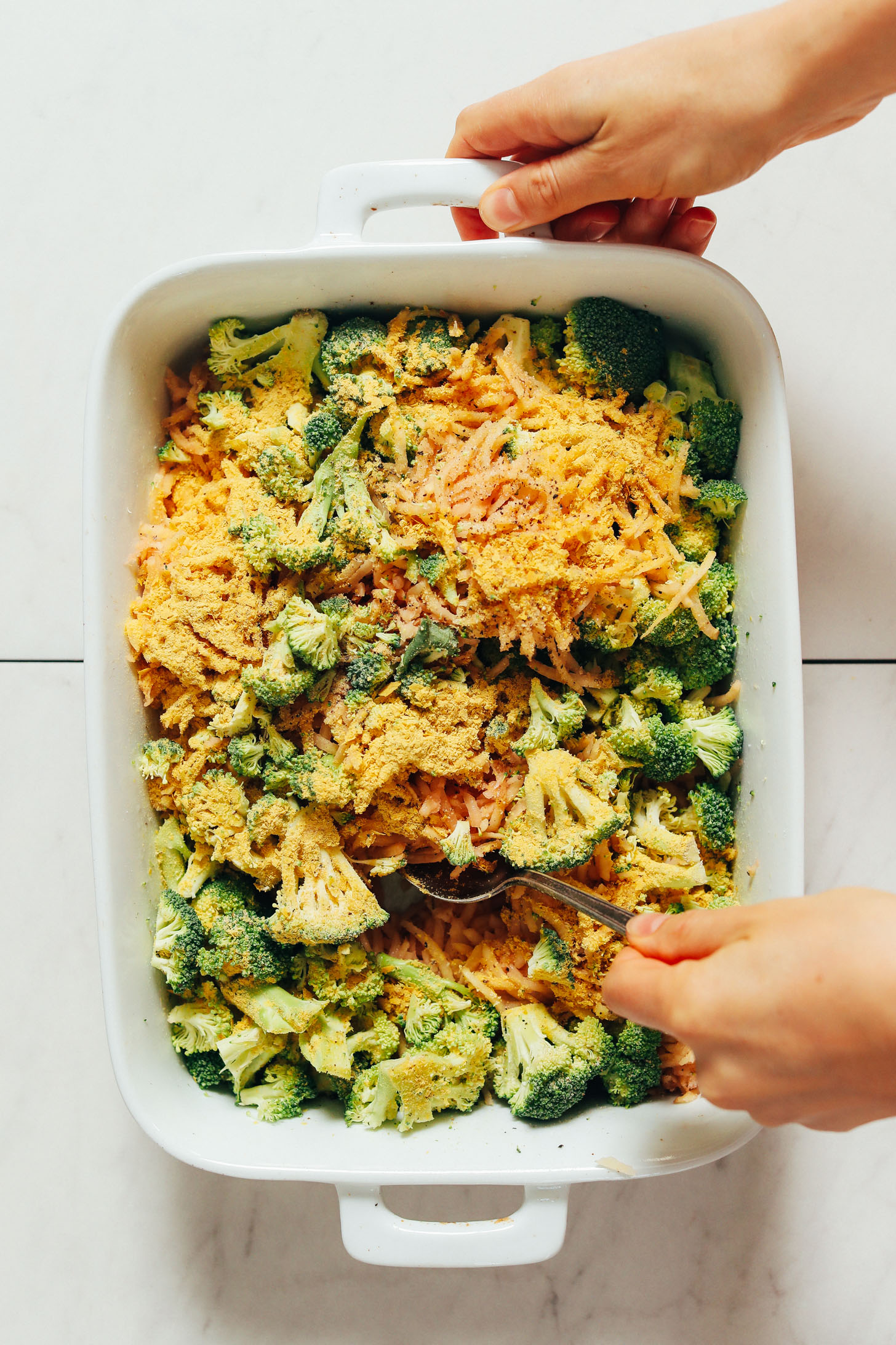 Holding a spoon and pan of our vegan broccoli hashbrown bake recipe