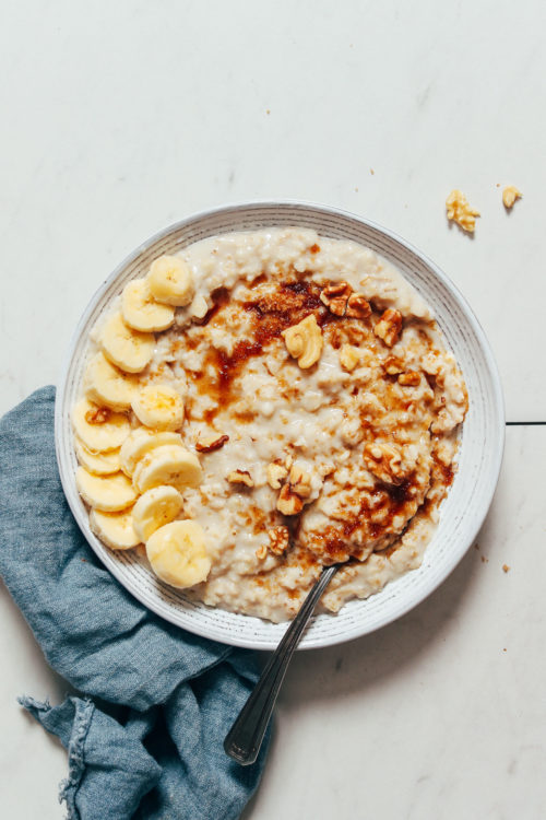 Bowl of rolled oats topped with banana, brown sugar, and walnuts