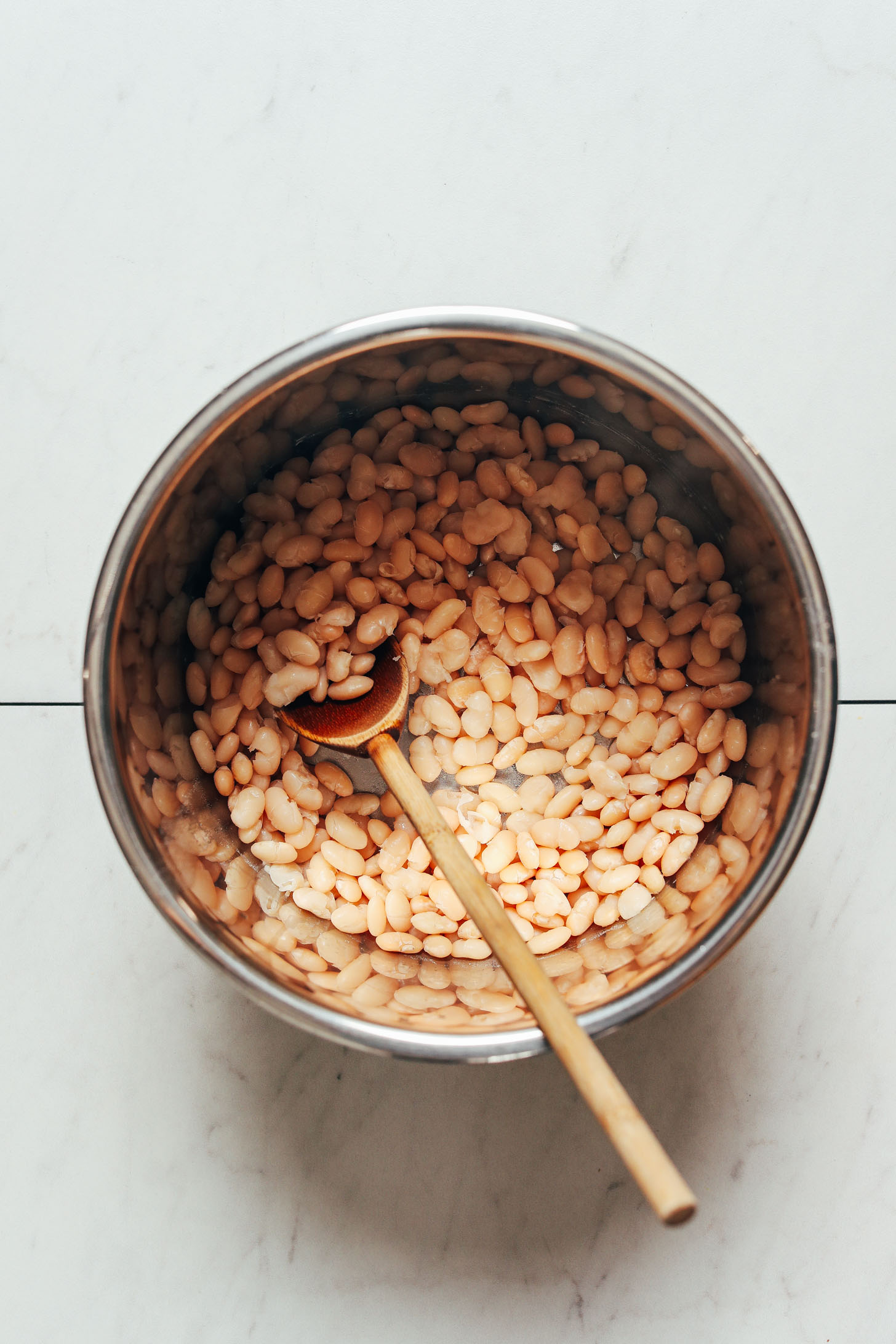Wooden spoon in an Instant Pot with cooked white beans