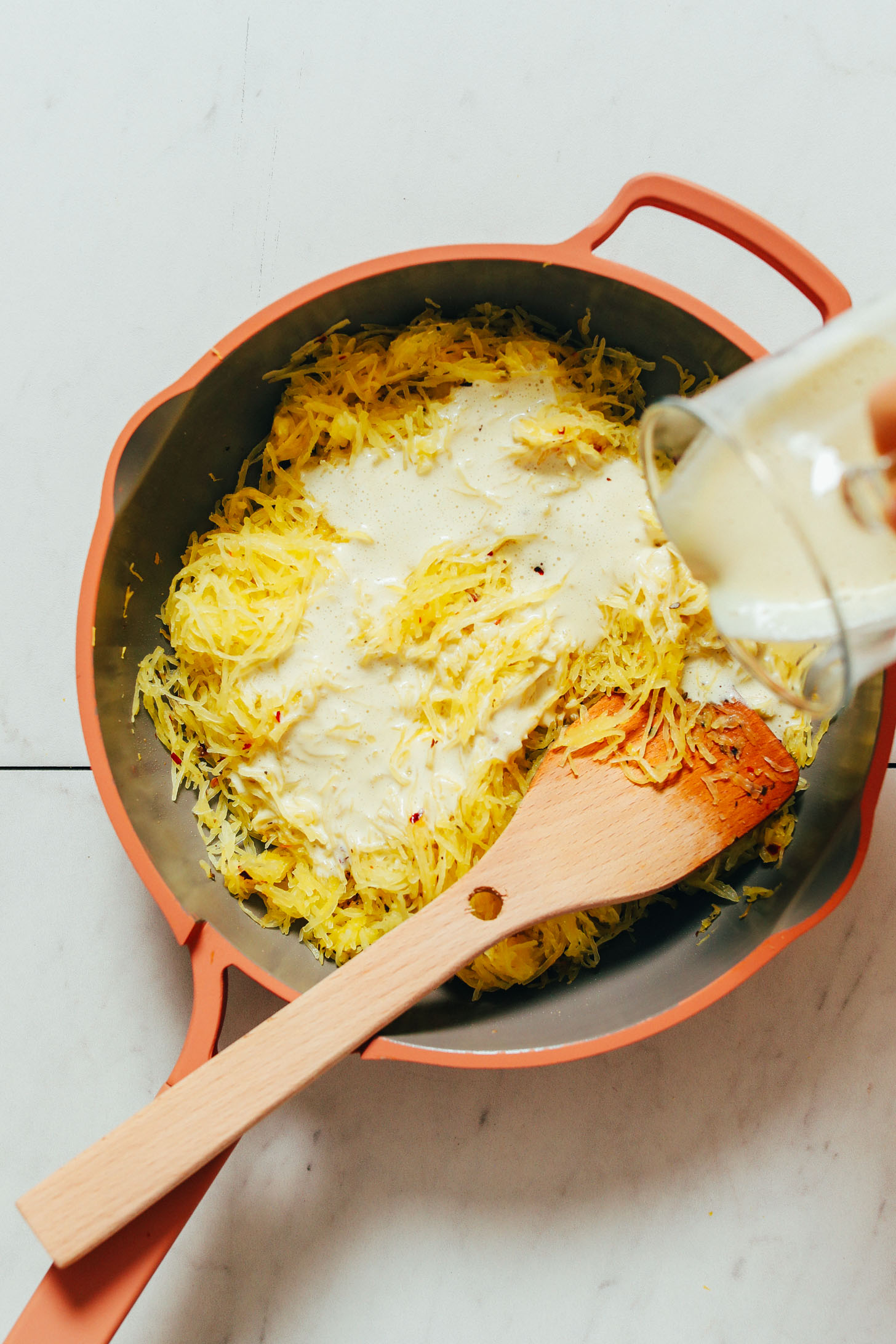 Pouring cashew sauce over spaghetti squash in the Always Pan