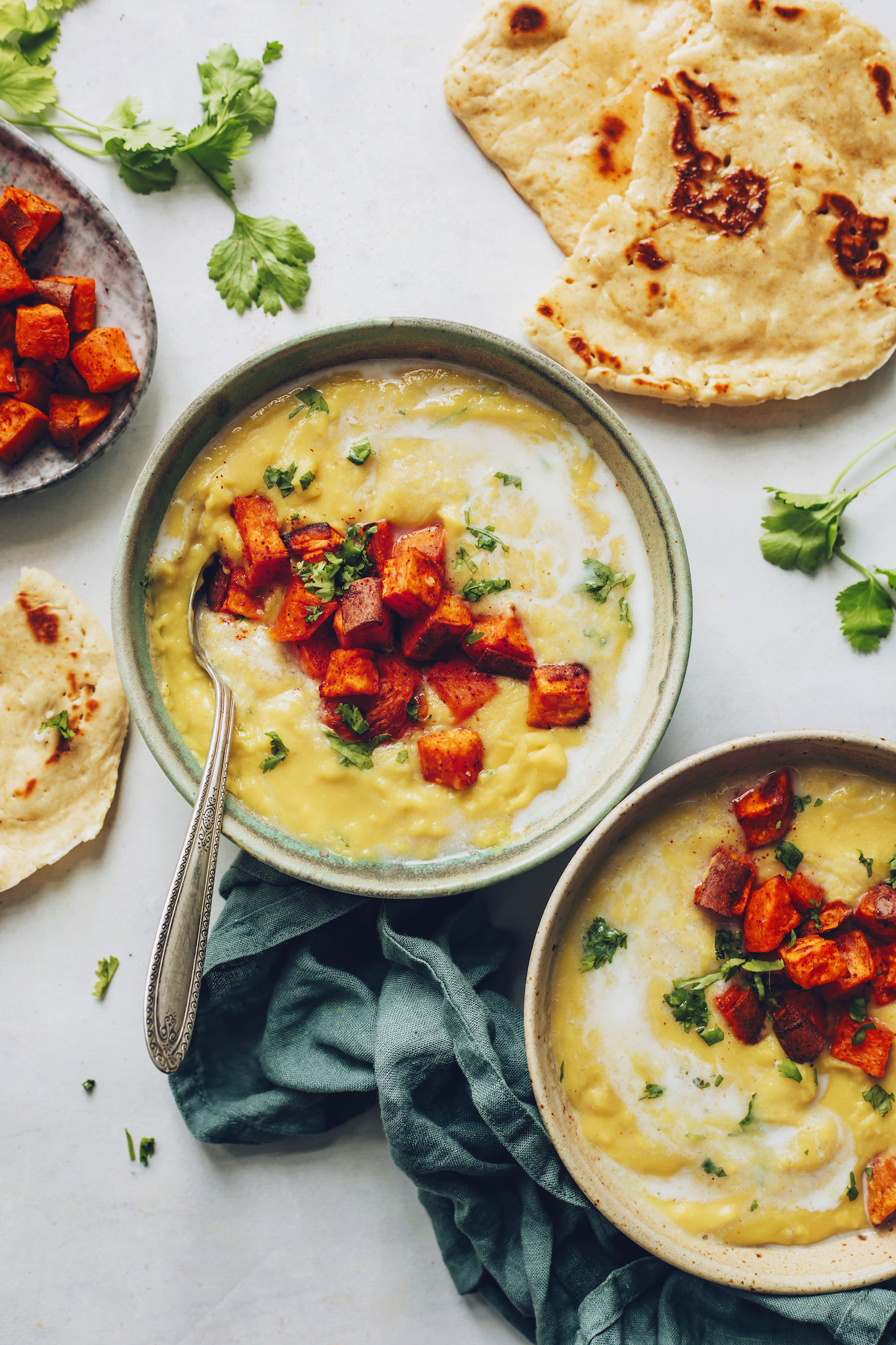 Two bowls of Instant Pot yellow split pea soup beside roasted sweet potatoes and naan