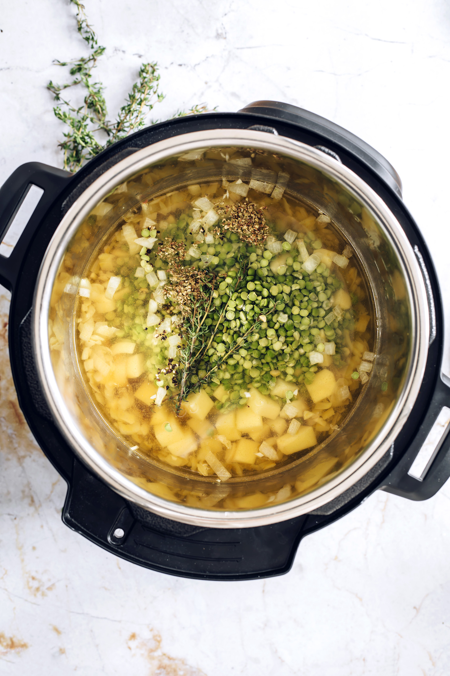Instant Pot with potatoes, onion, garlic, green split peas, thyme, and oregano