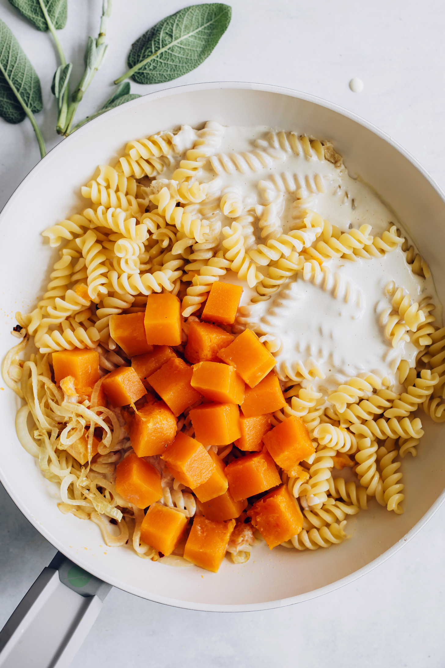 Skillet of cooked pasta, caramelized onion, butternut squash, and garlicky vegan alfredo