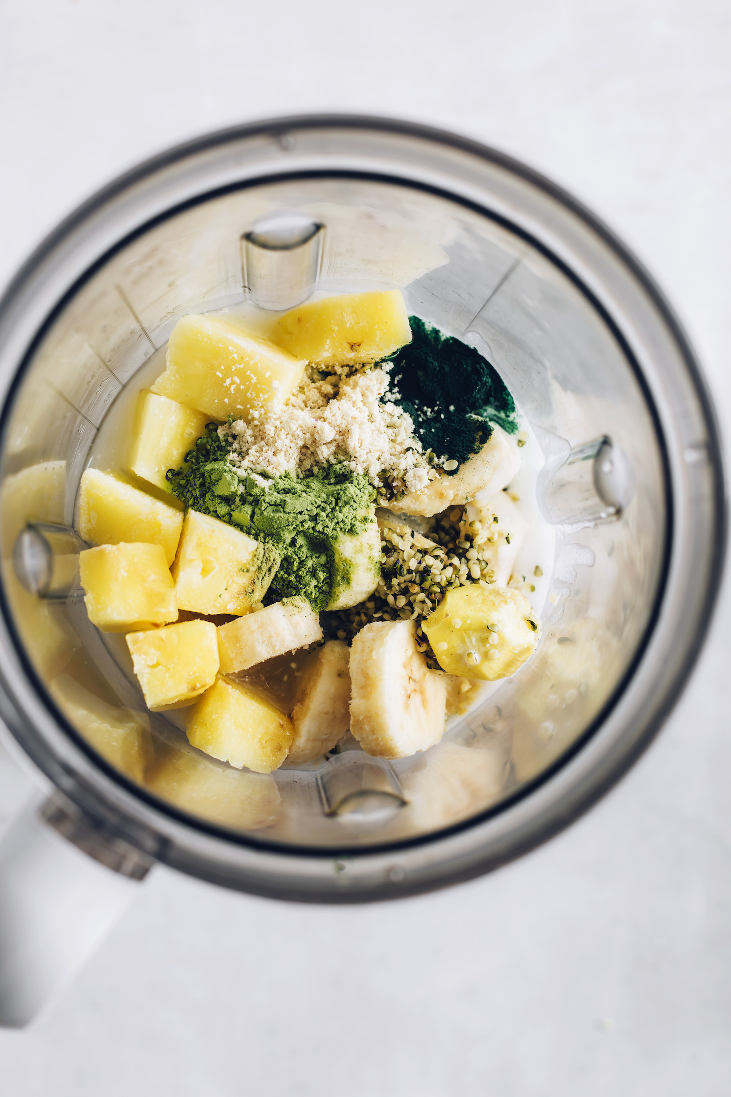 Frozen pineapple, banana, hemp seeds, dairy-free milk, and superfood powders in a blender