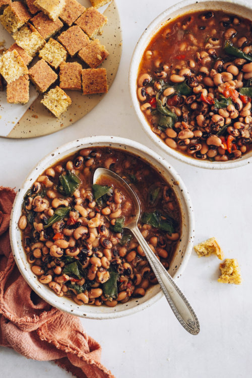 Two bowls of Instant Pot Black Eyed Peas and Greens with vegan cornbread