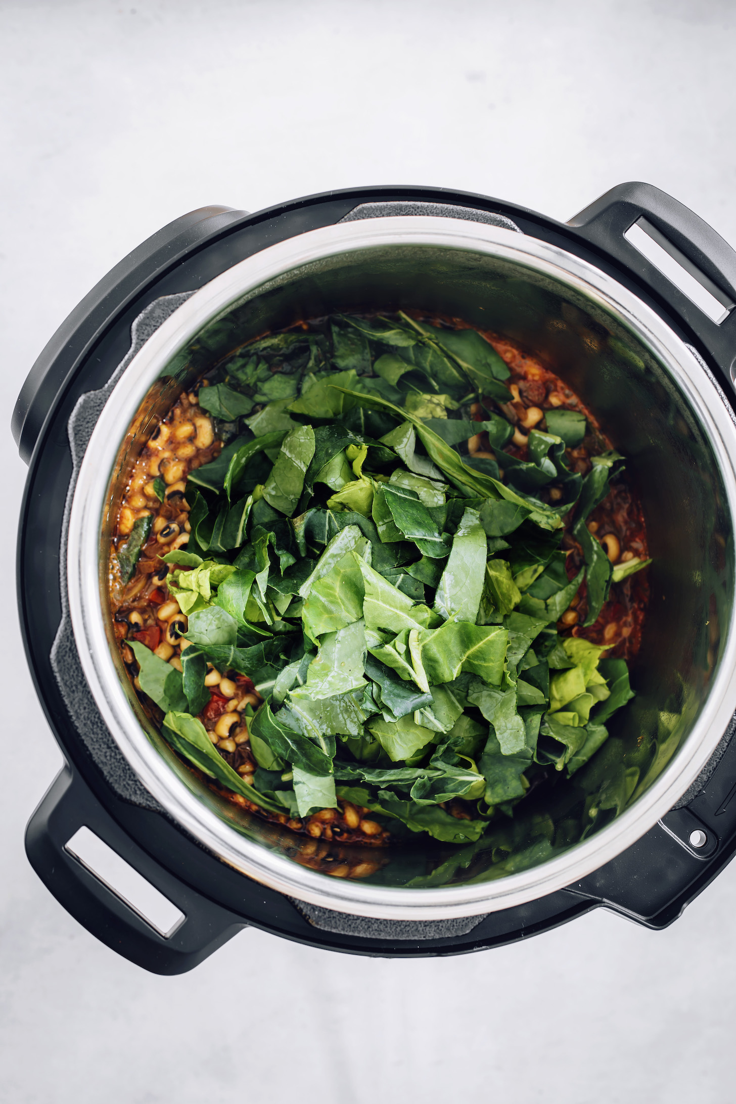 Chopped collard greens in an Instant Pot over seasoned black eyed peas