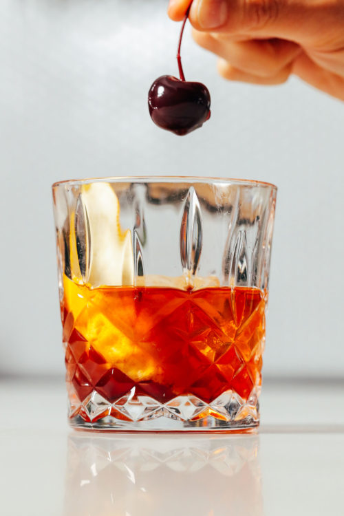 Holding a cocktail cherry over an Old Fashioned