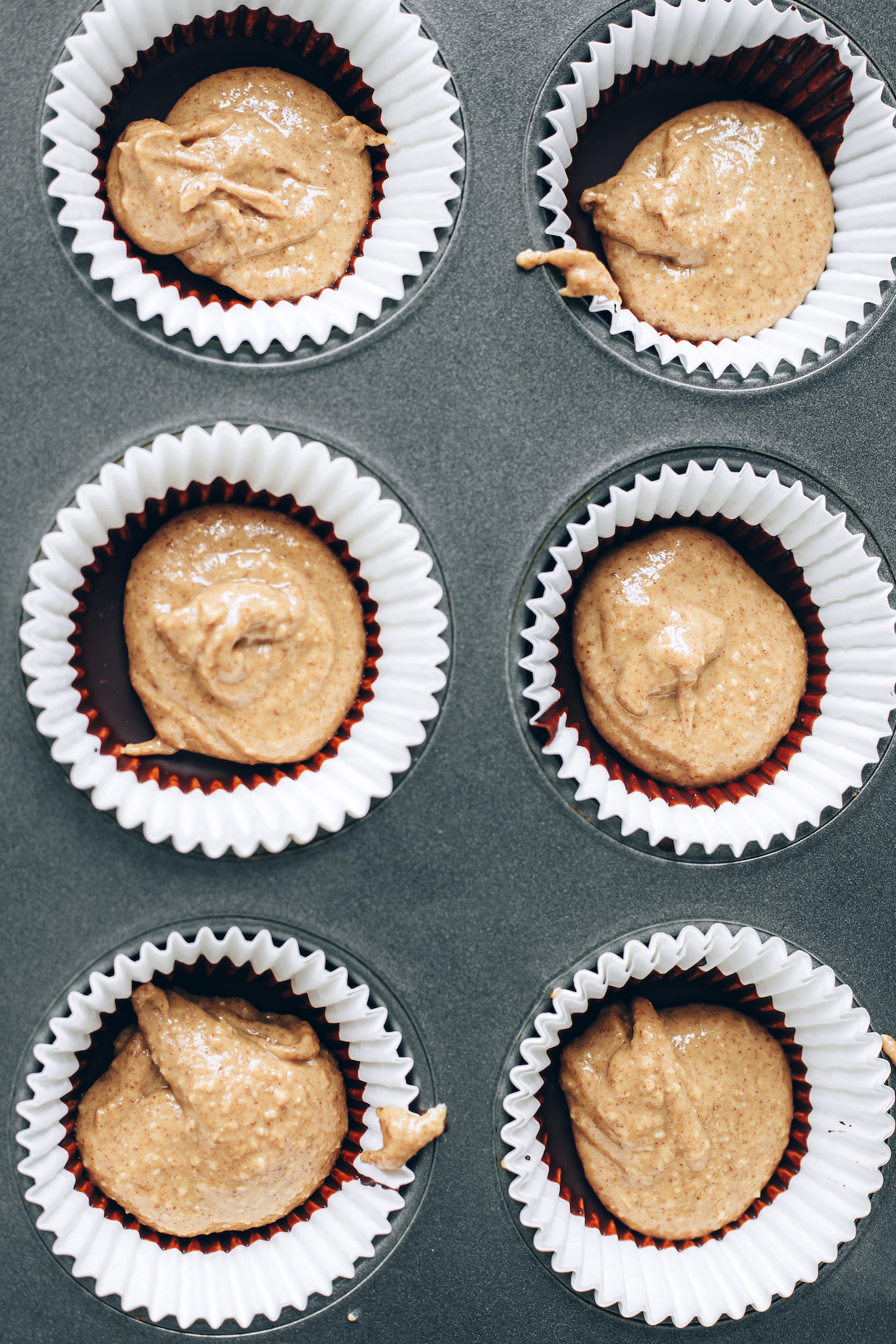 Mini muffin tin with paper liners filled with melted chocolate and peanut butter