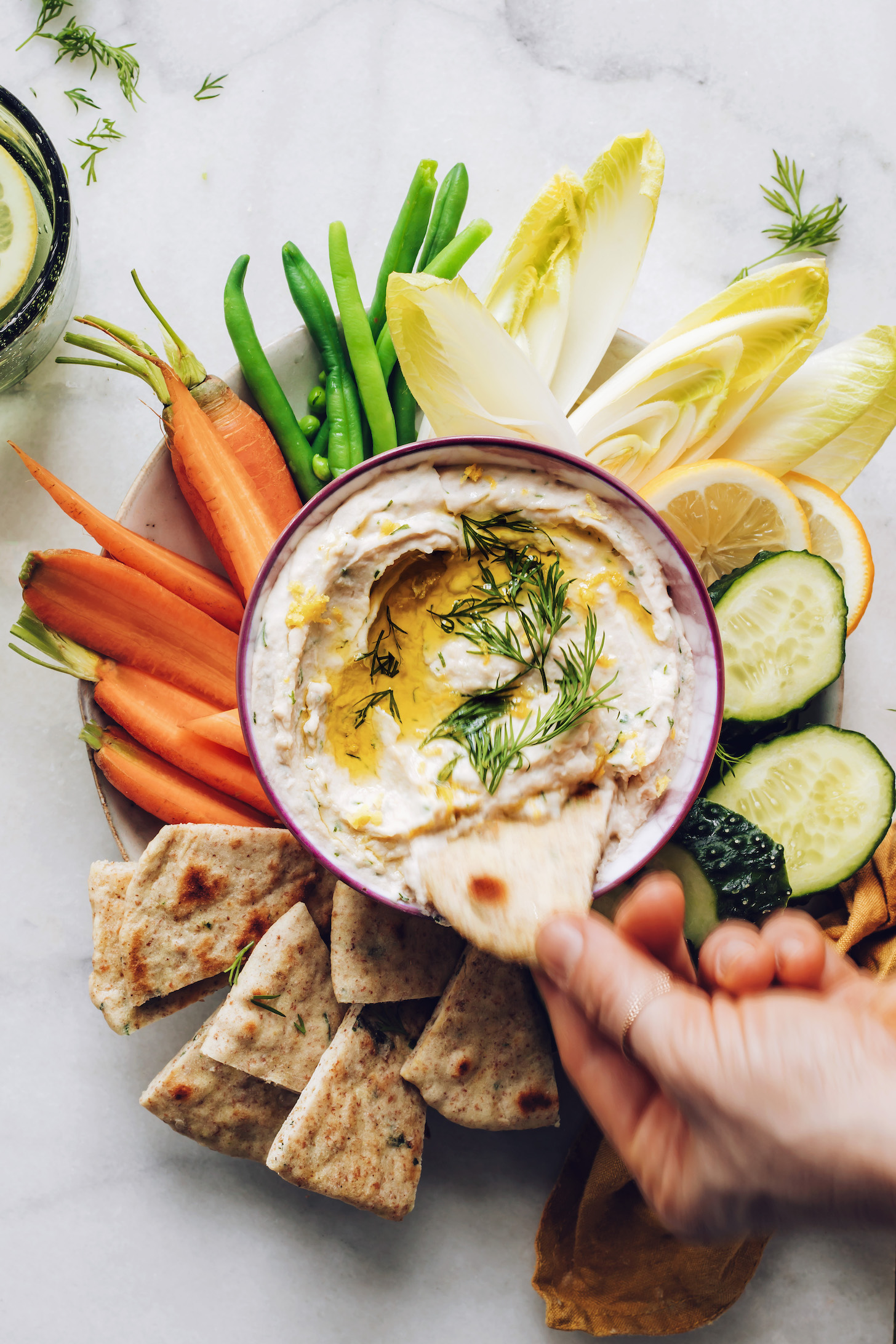 Dipping a slice of pita bread into our lemon and herb white bean hummus recipe