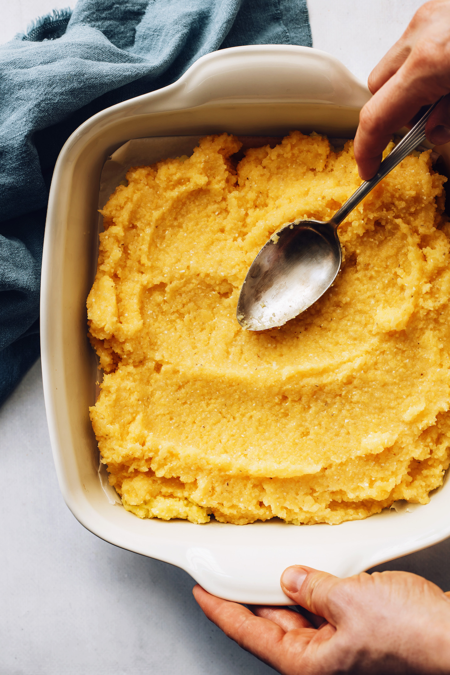 Using a spoon to smooth over the top of a pan of polenta