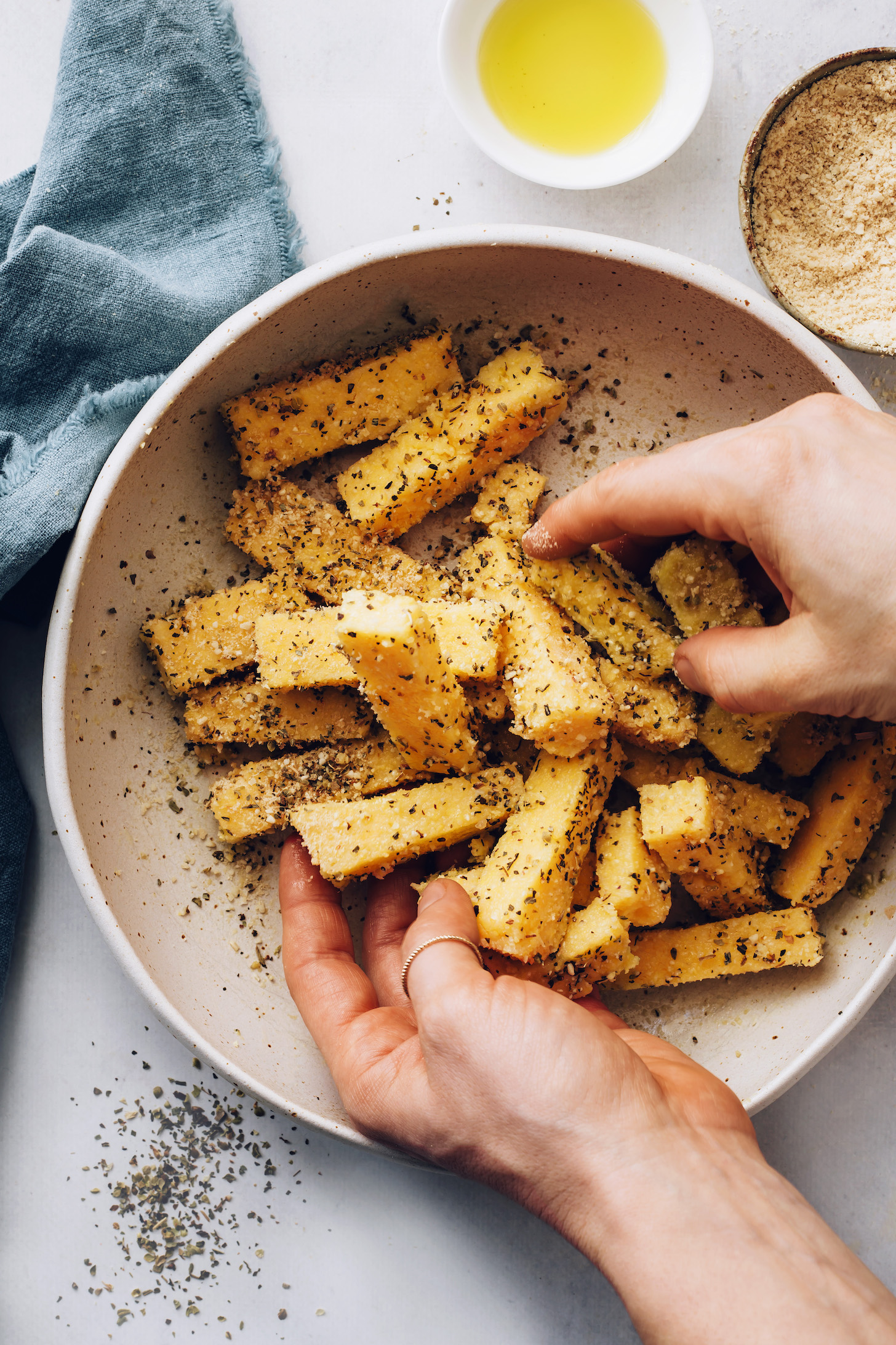 Tossing polenta fries in a bowl with olive oil, Italian herbs, and vegan parmesan