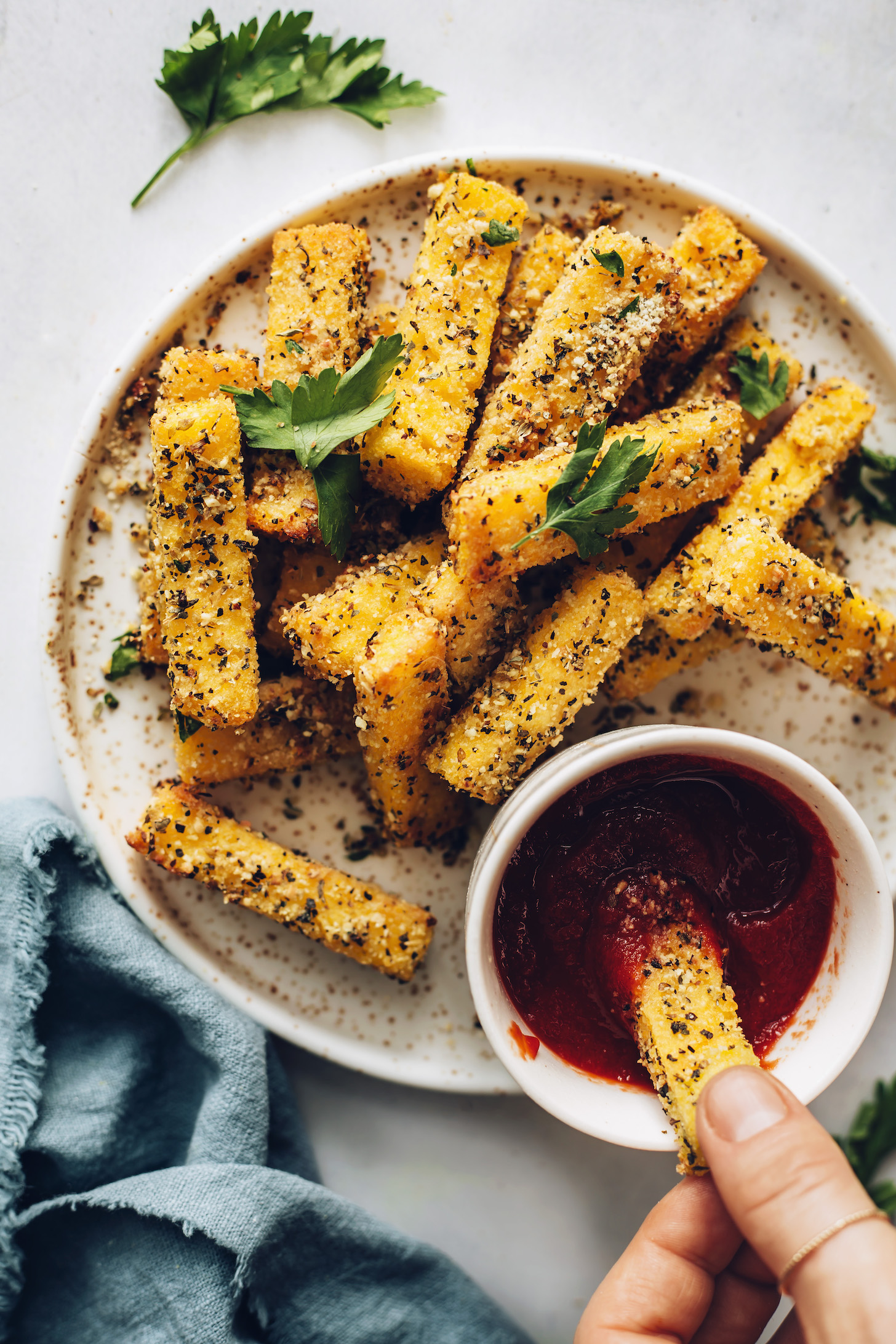 Plate of polenta fries with one being dipped in a bowl of marinara