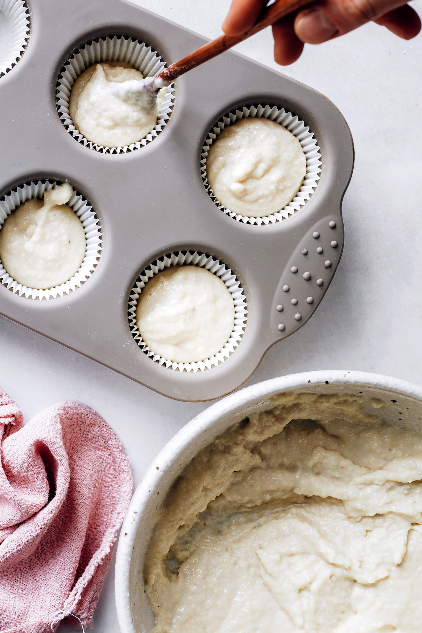 Scooping vegan vanilla cupcake batter into a parchment-lined muffin tin