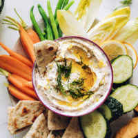 Bowl of white bean hummus surrounded by fresh vegetables and pita bread