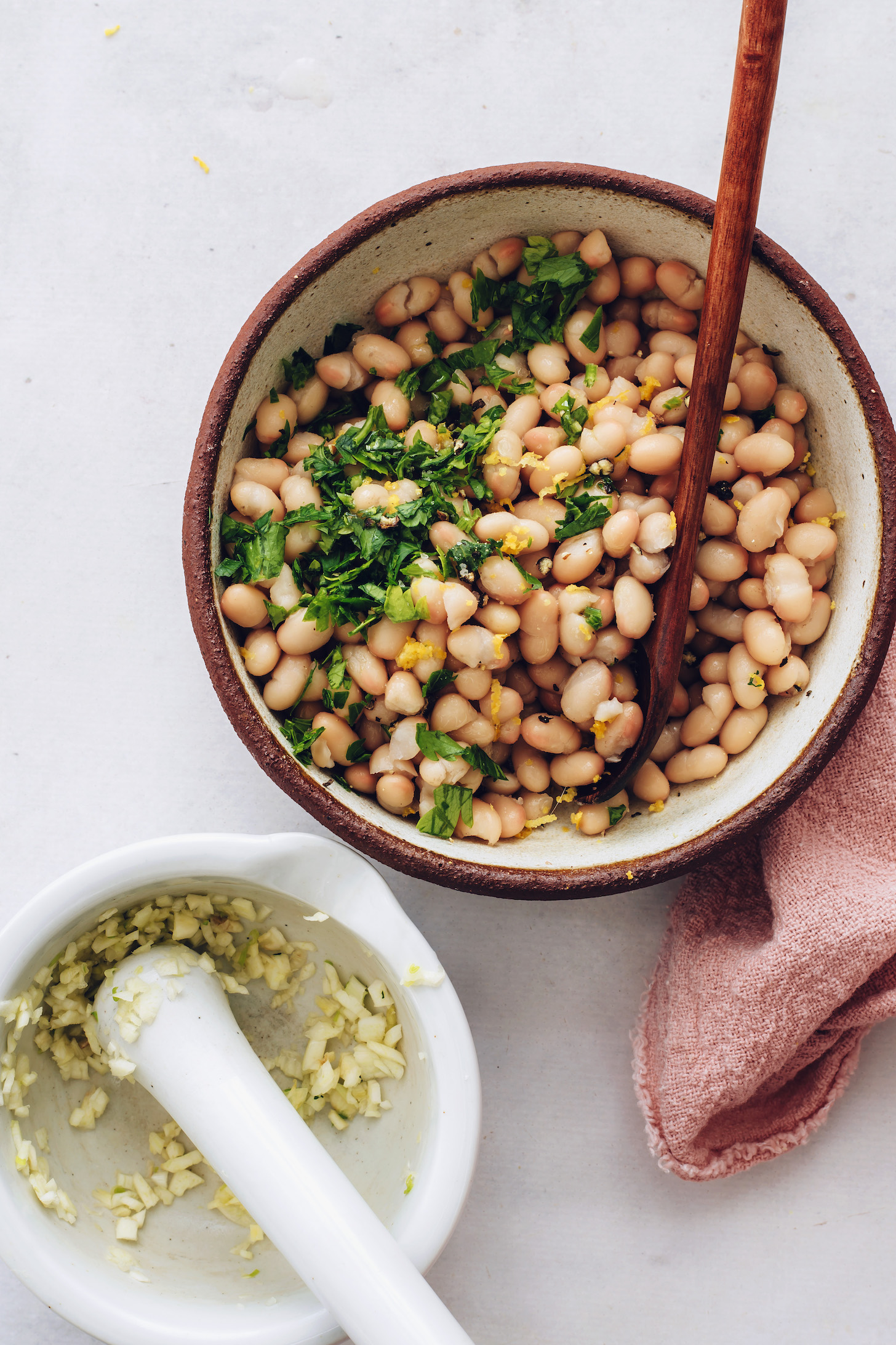 Bowls of minced garlic and white beans with parsley and lemon zest