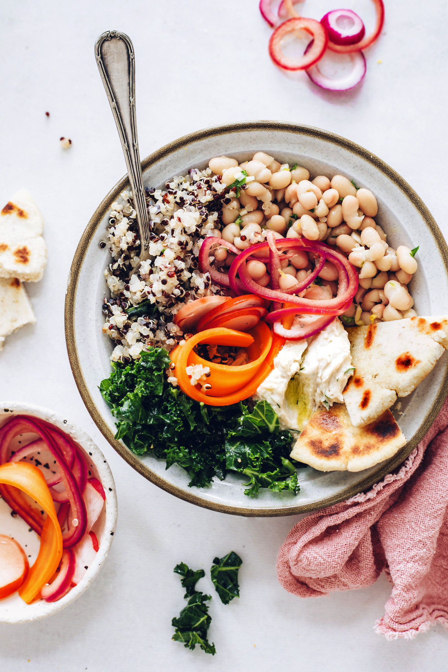 Bowl of cooked quinoa, white beans, GF flatbread, hummus, pickled veggies, and massaged kale