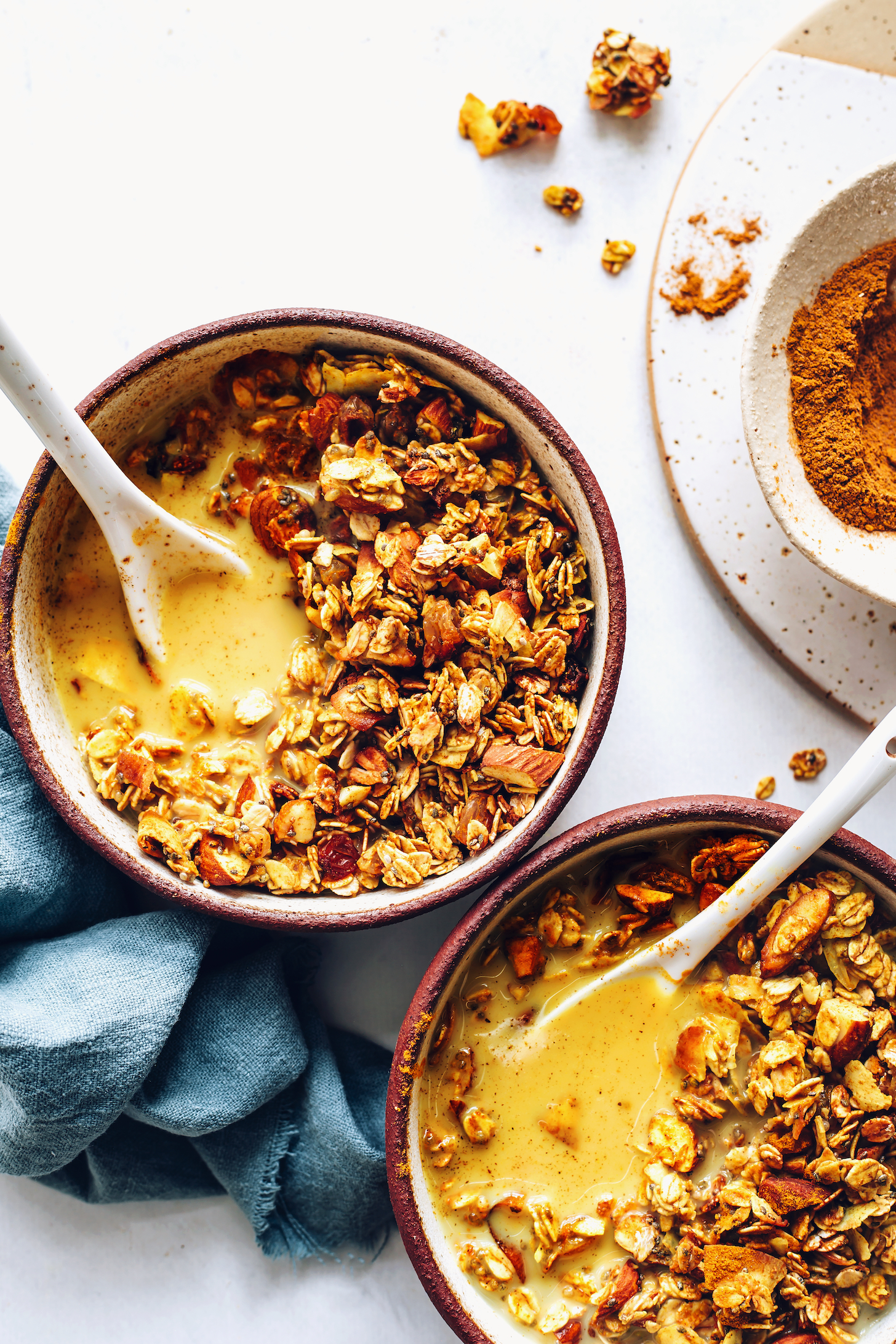 Bowl of golden milk spice mix next to two bowls of golden milk granola with dairy-free milk