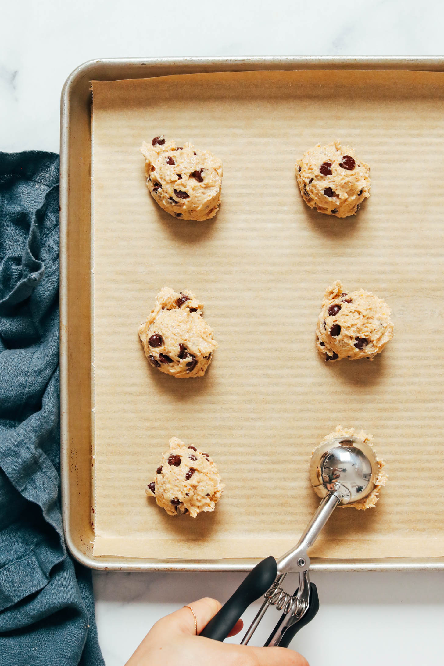 Scooping balls of chocolate chip cookie dough on a parchment-lined baking sheet