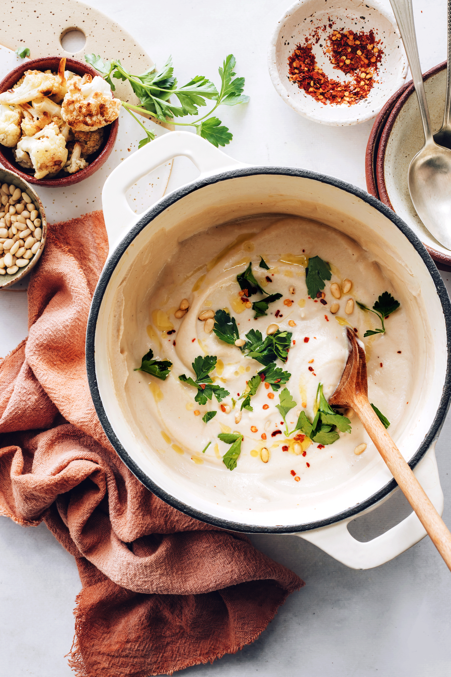 Large pot of roasted cauliflower soup topped with red pepper flakes, pine nuts, and parsley