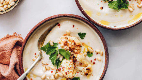 Two bowls of vegan cauliflower soup topped with parsley, pine nuts, and roasted cauliflower