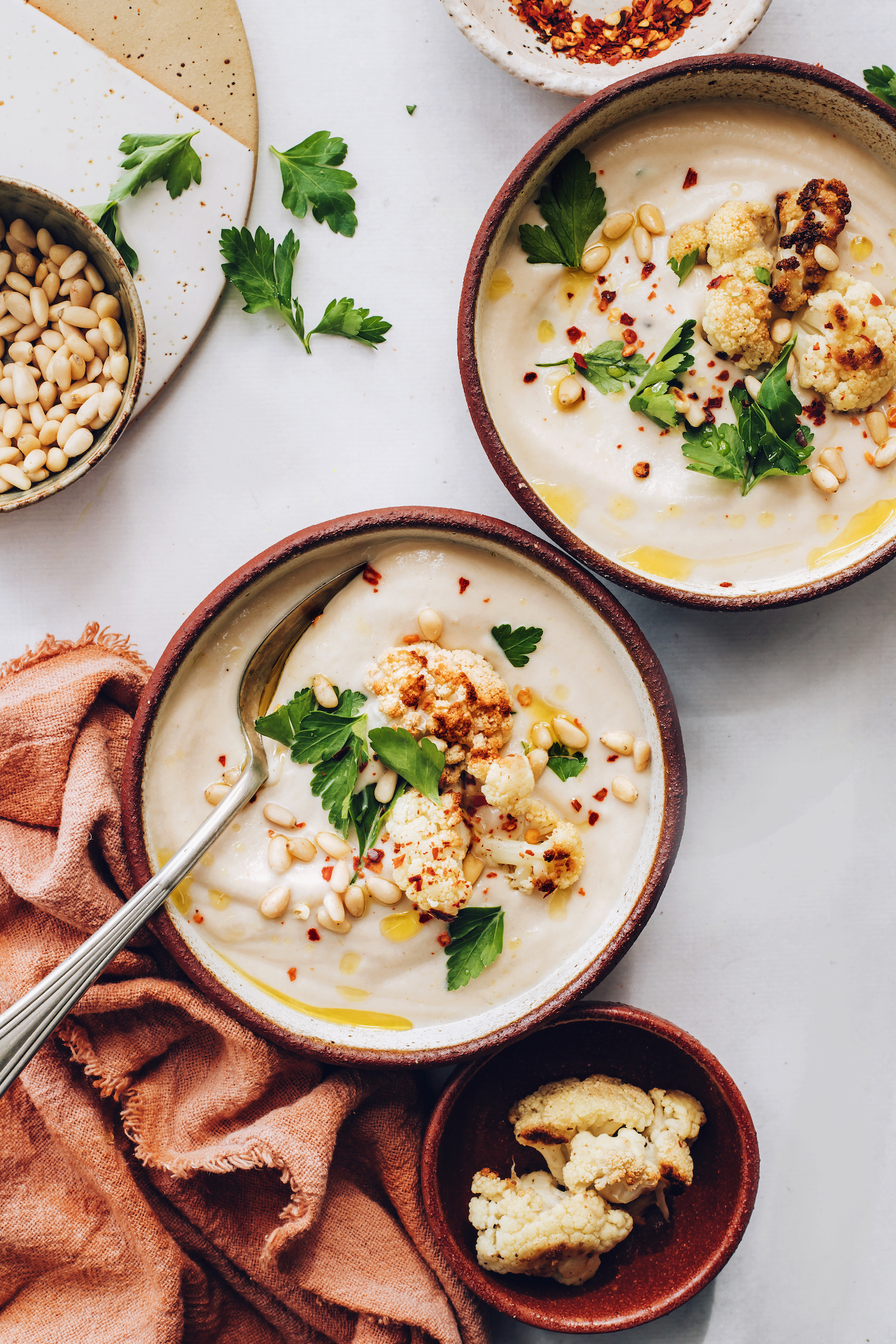 Two bowls of vegan cauliflower soup topped with parsley, pine nuts, and roasted cauliflower