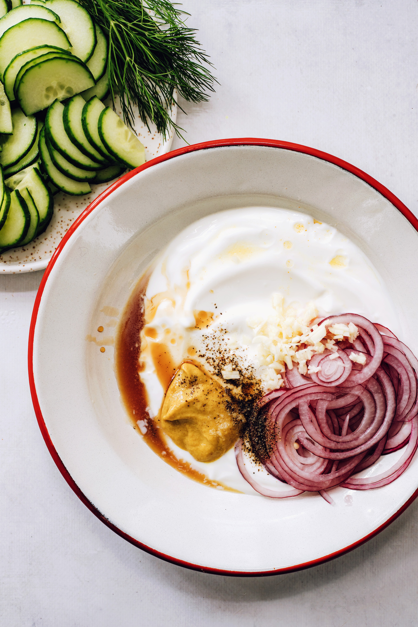 Sliced cucumber and dill beside a bowl of creamy coconut yogurt dressing