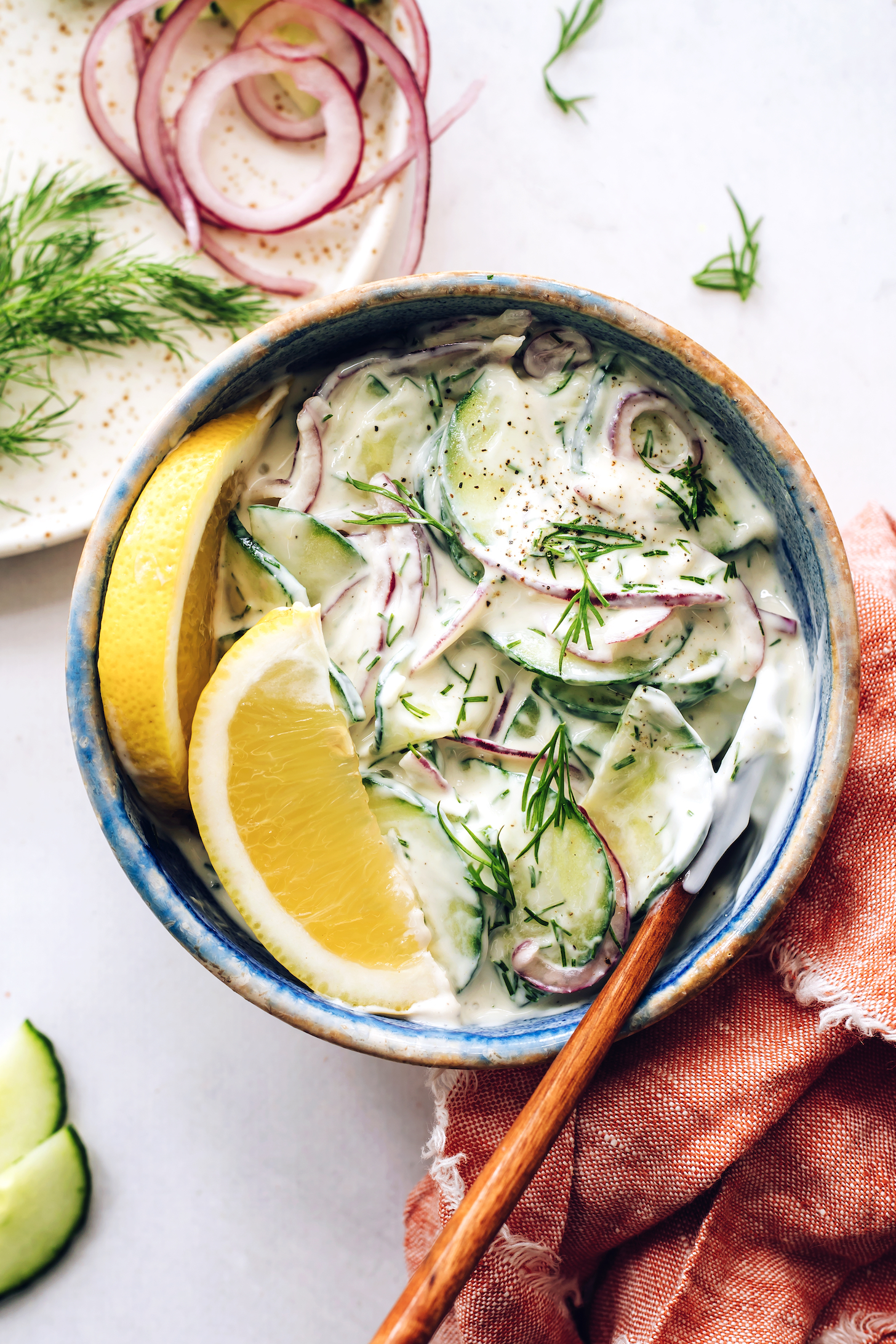 Bowl of creamy cucumber salad topped with lemon wedges and fresh dill
