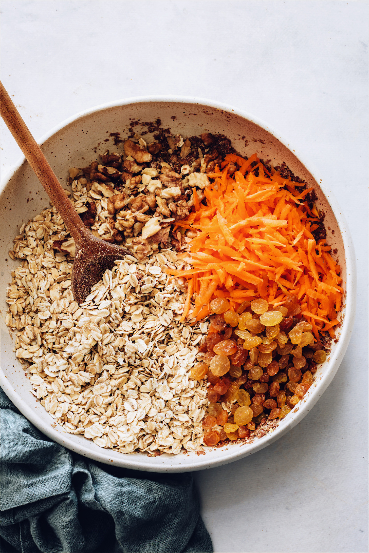 Bowl of wet ingredients topped with oats, walnuts, raisins, and carrots
