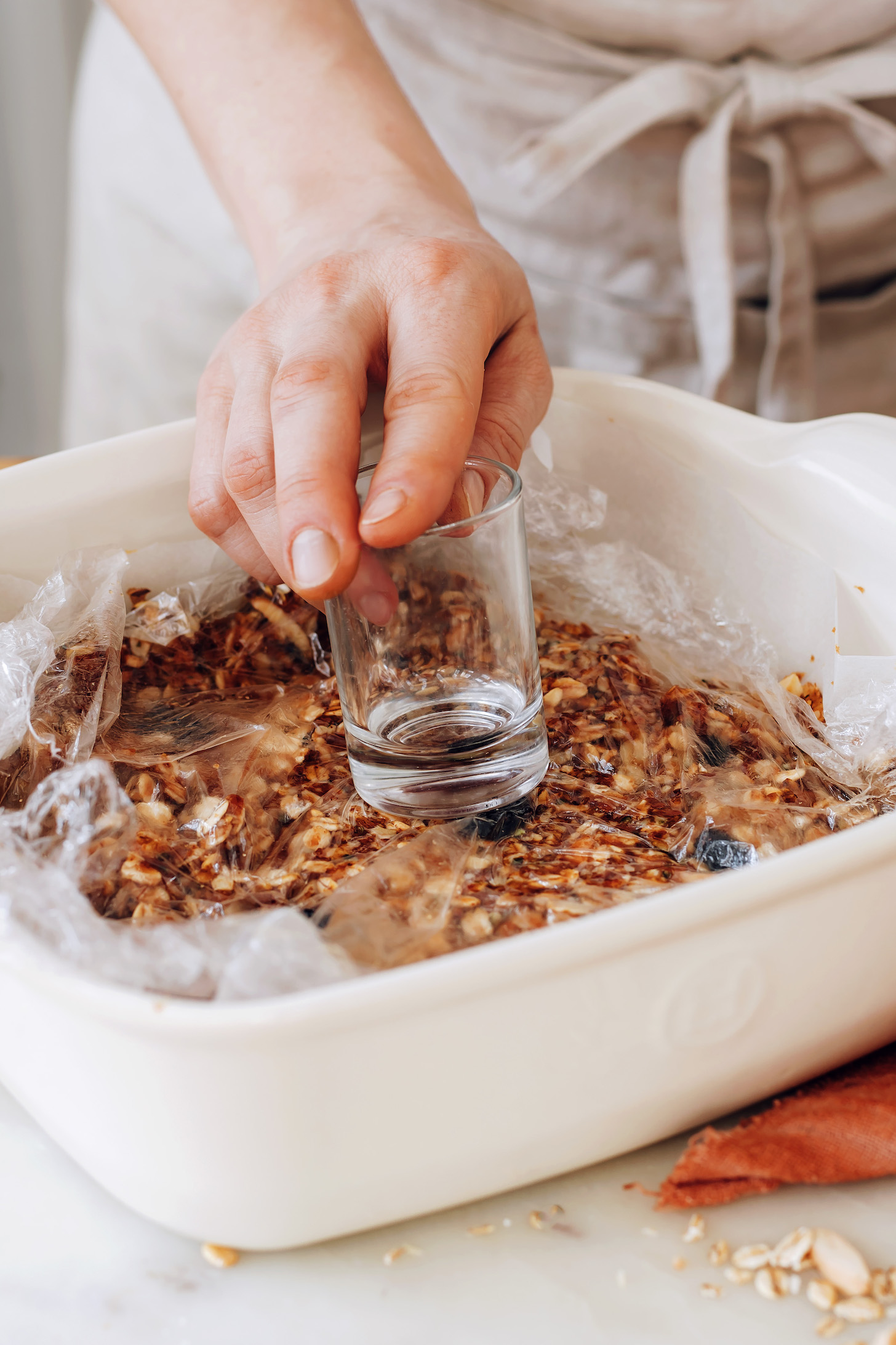 Using a glass to press no-bake granola bars into a pan