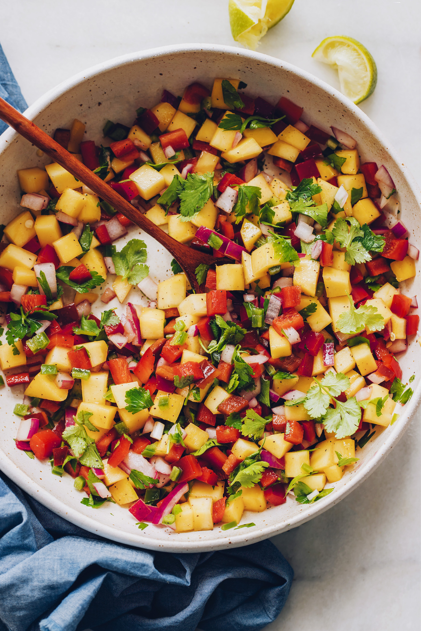 Wooden spoon in a big bowl of mango salsa
