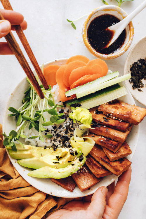Holding chopsticks over a vegan sushi bowl with ginger marinated tofu