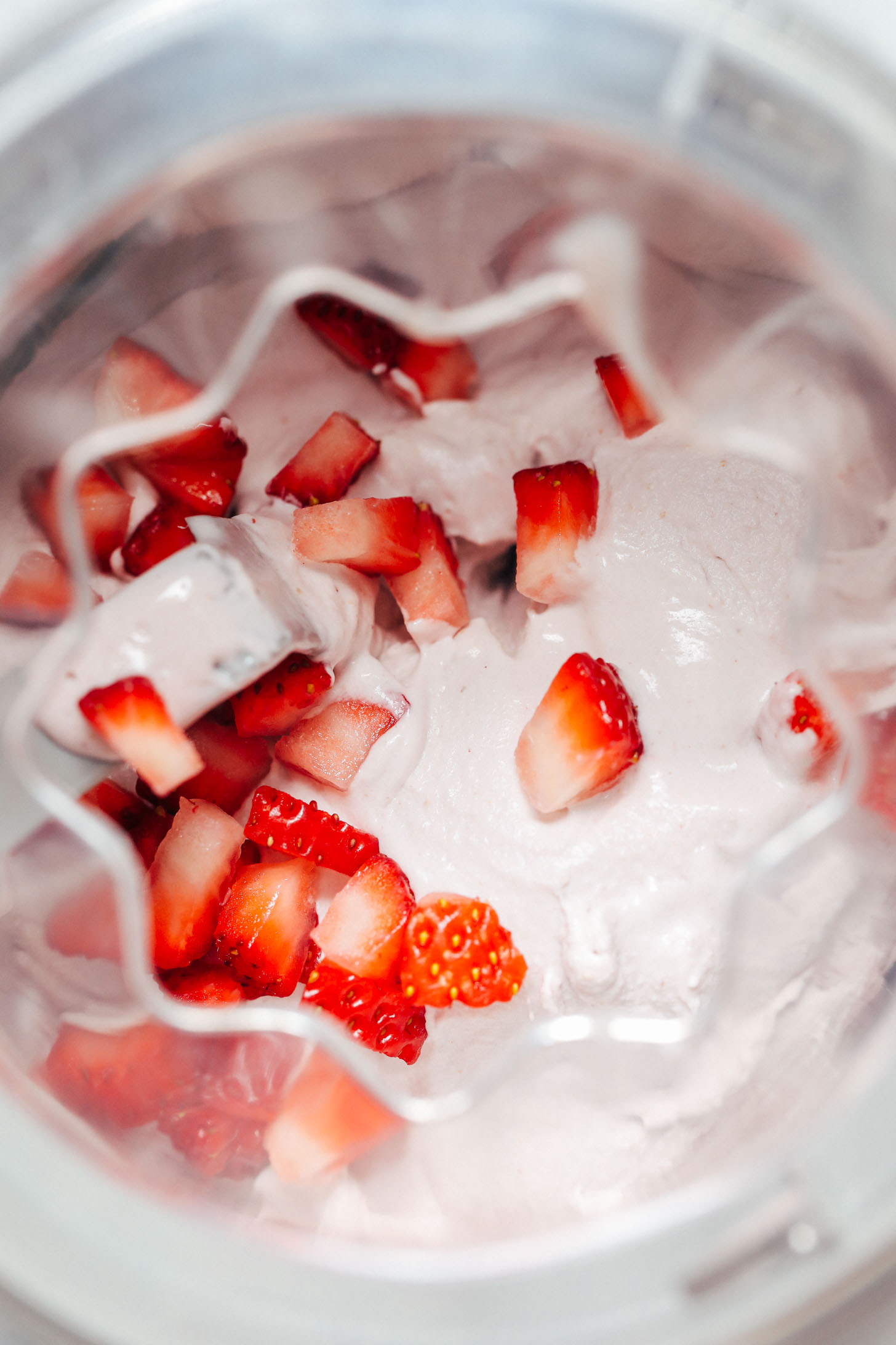 Ice cream churner with vegan strawberry ice cream topped with chopped fresh strawberries