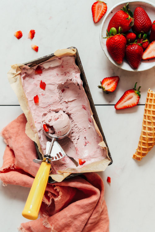 Ice cream scoop in a pan of vegan strawberry ice cream