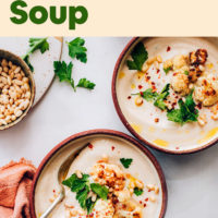 Bowls of vegan and gluten-free roasted cauliflower soup with pieces of roasted cauliflower, cilantro, and pine nuts