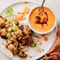Dipping roasted cauliflower in a bowl of harissa tahini sauce