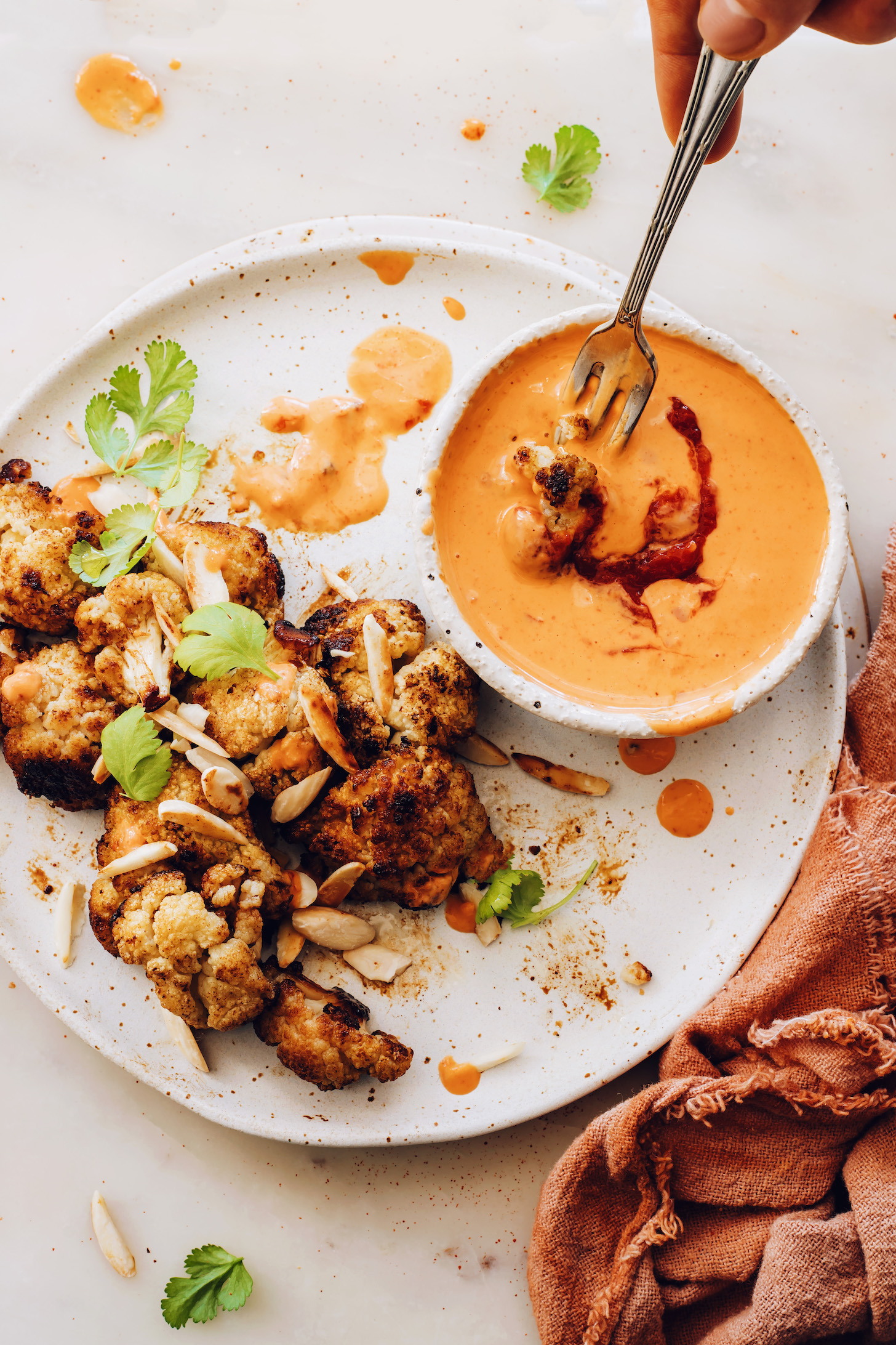 Dipping a piece of roasted cauliflower in a bowl of harissa tahini sauce