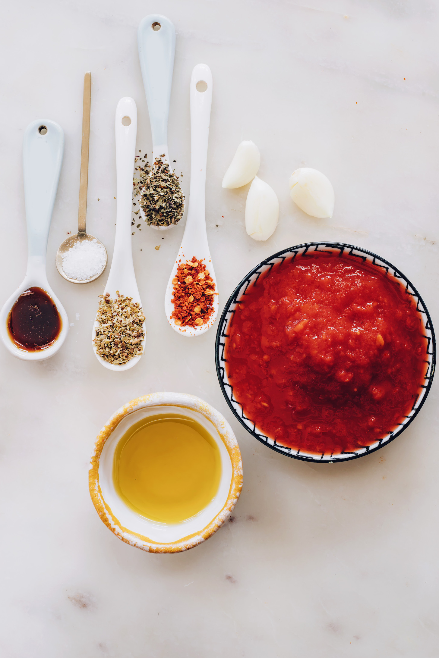 Karanfil sarımsak, kaşık dolusu ot, kırmızı pul biber, tuz ve akçaağaç şurubu ve kaseler zeytinyağı ve ezilmiş domates