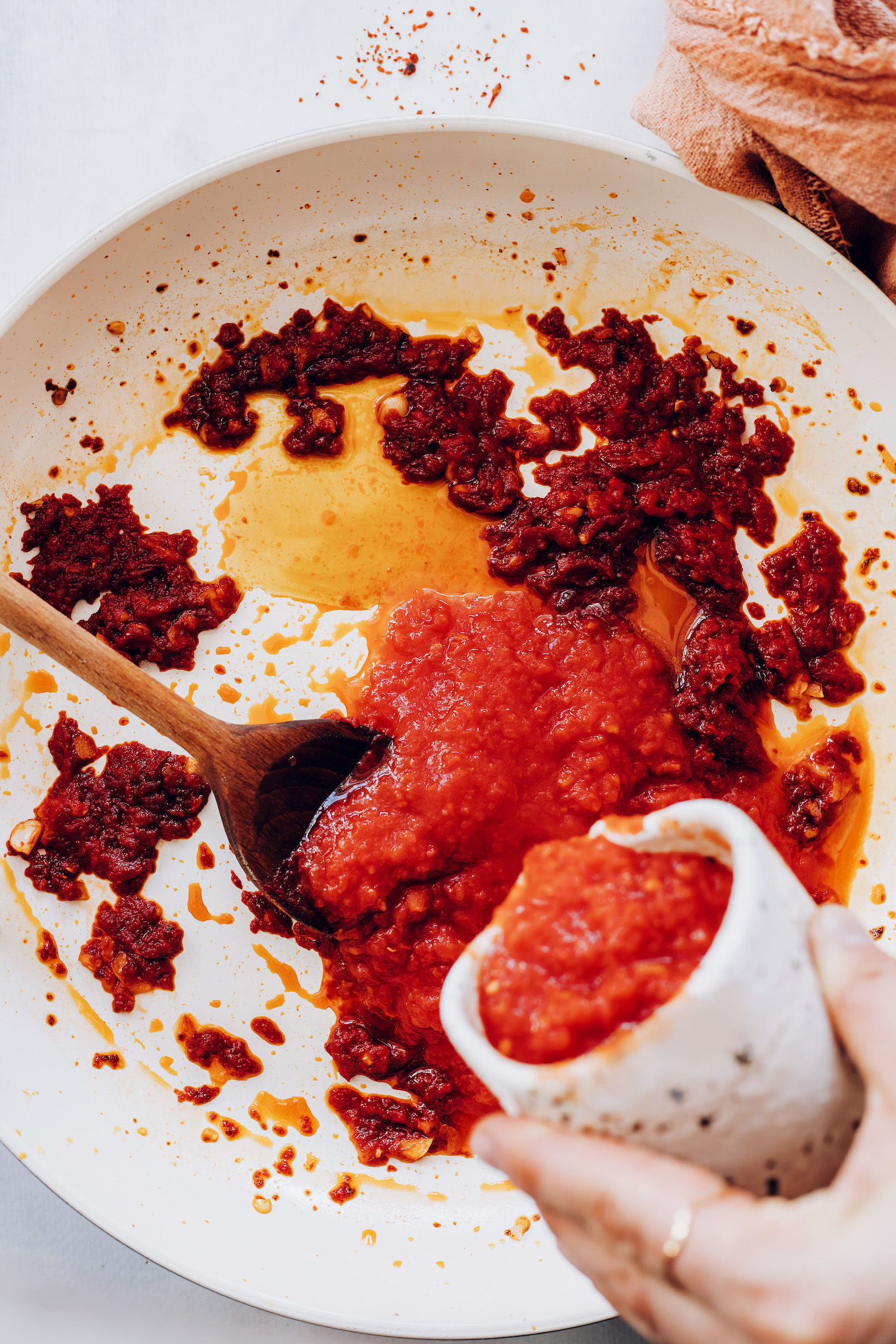 Pouring crushed tomatoes into a skillet of sautéed red pepper flakes, garlic, and tomato paste
