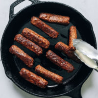 Flipping a vegan sausage link cooking in a cast iron skillet