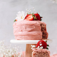 Slice of vegan gluten-free strawberry cake on a small plate in front of the whole cake