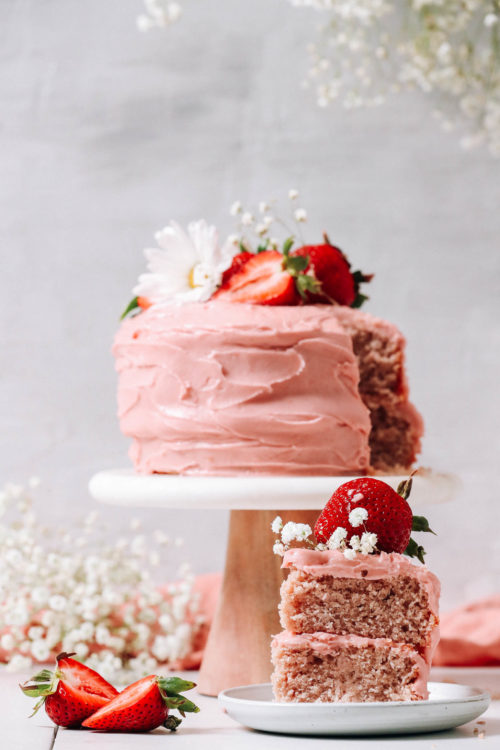 Slice of vegan gluten-free strawberry cake on a small plate in front of the whole cake