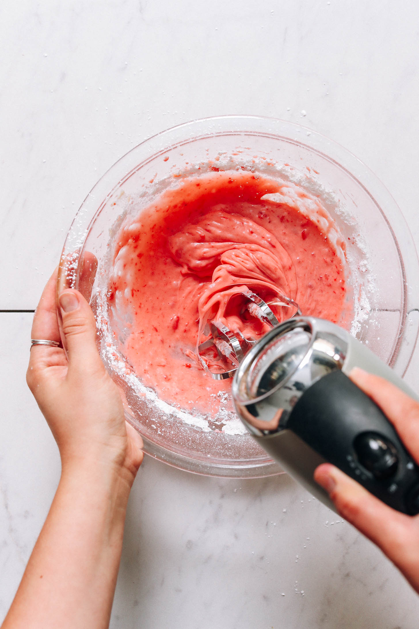 Using a hand mixer to whip strawberry frosting