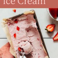 Pan of creamy vegan strawberry ice cream with a scoop in it, and fresh strawberries