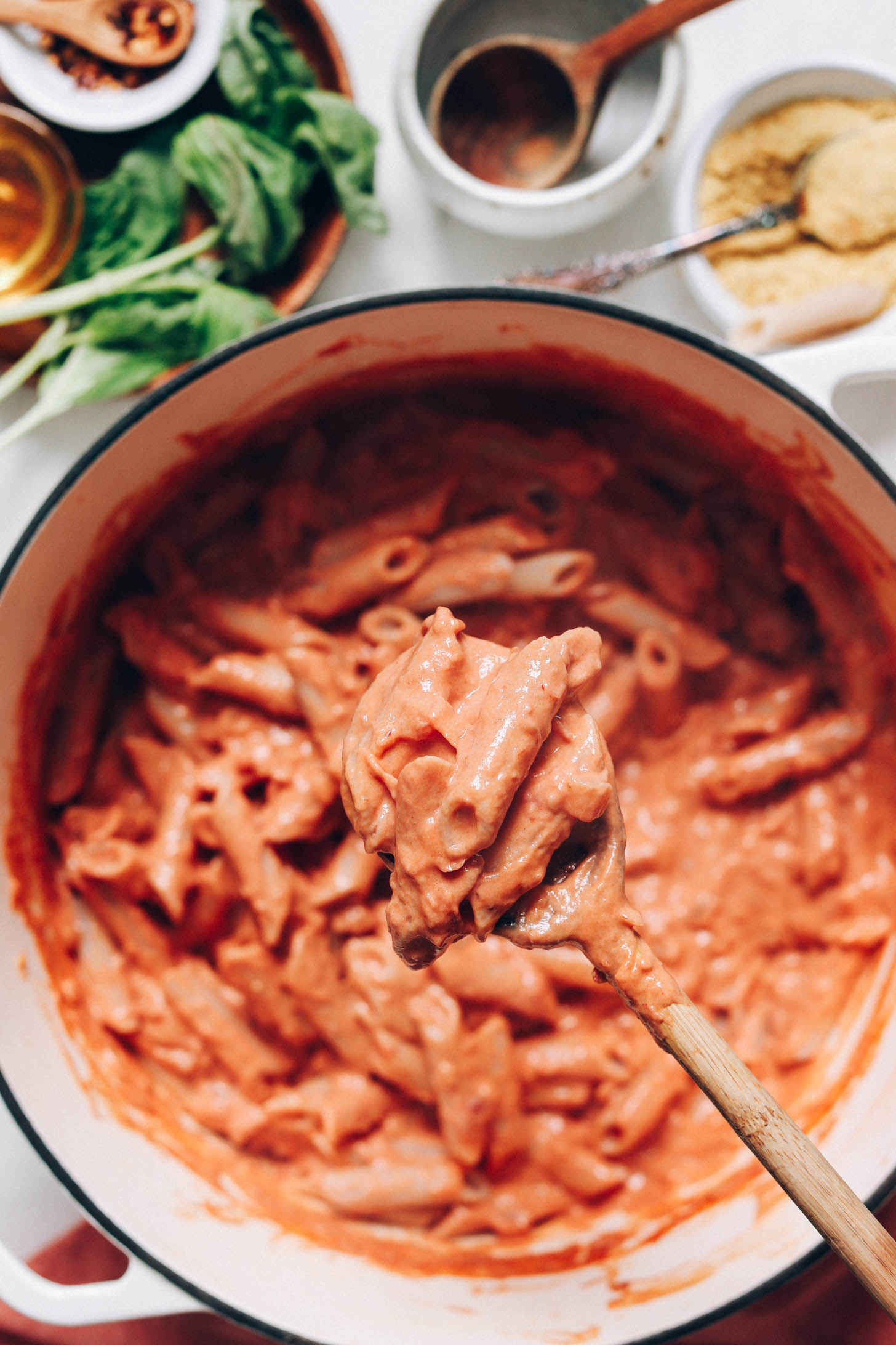 Holding a spoonful of vegan pink penne pasta above a Dutch oven with more pasta