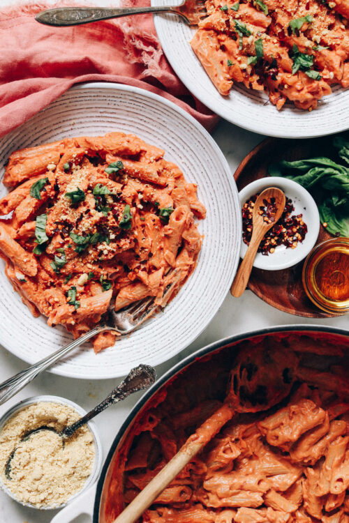 Bowls and pan of vegan pink pasta topped with basil and vegan parmesan