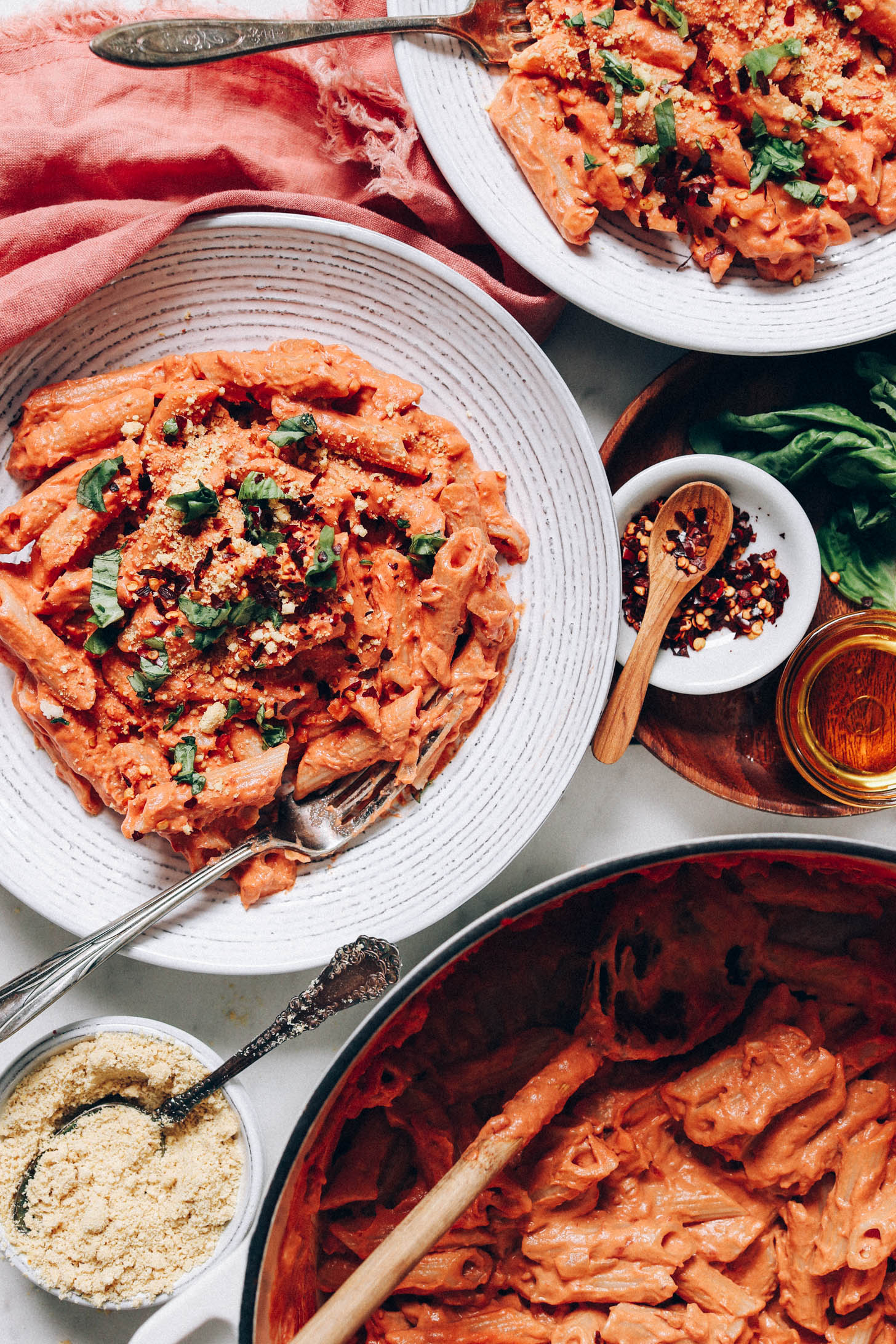 Two bowls of creamy vegan pink pasta next to a skillet with more pasta