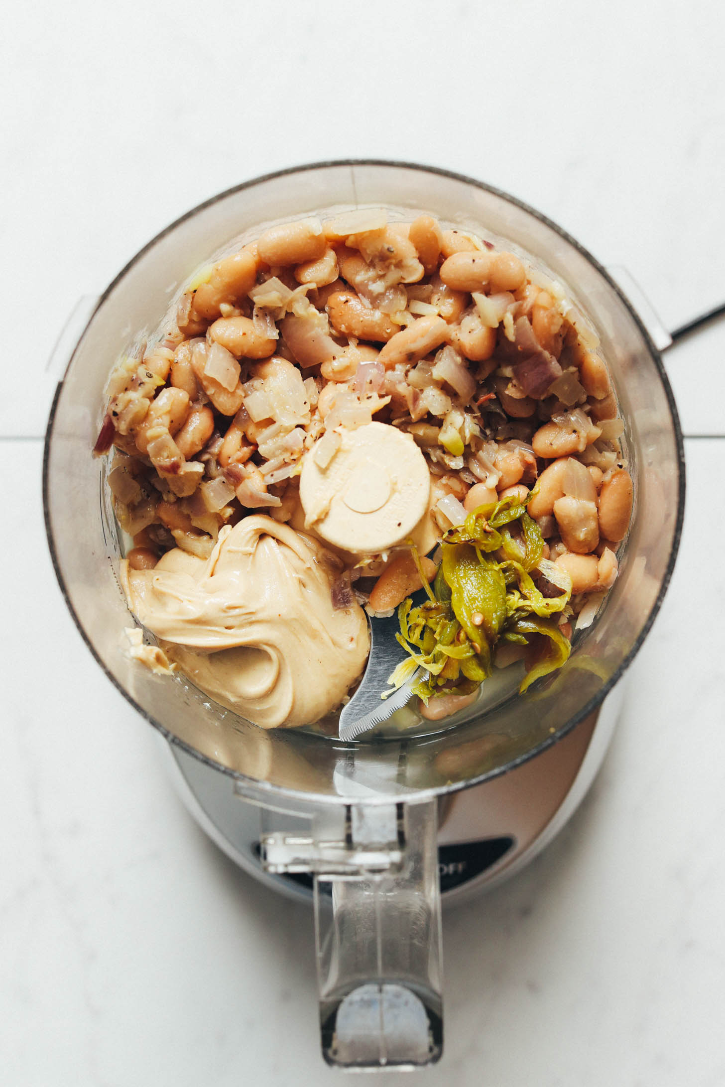 Food processor with white beans, sautéed shallot and garlic, roasted serranos, cashew butter, lemon juice, and salt and pepper