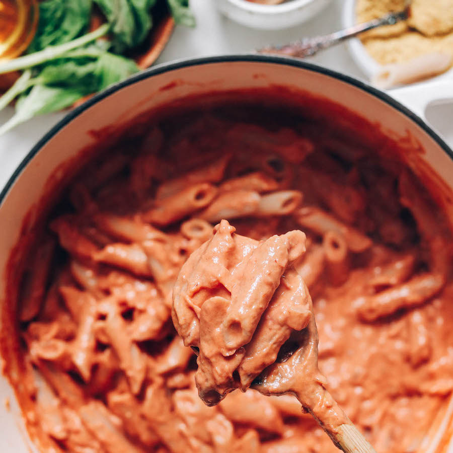 A wooden spoon holding vegan pink pasta on top of a pan
