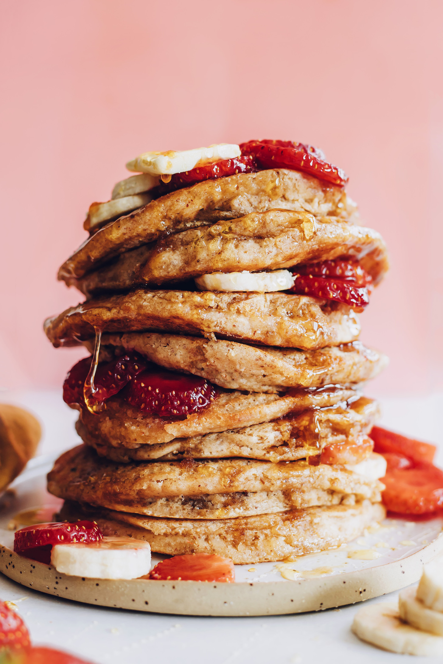 Stack of gluten-free pancakes topped with fresh fruit and maple syrup